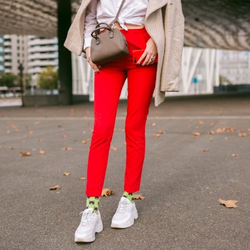 Close up fashion details , young woman wearing trendy red pants funny socks and ugly fashion sneakers, beige elegant coat, posing on the street near business centers, autumn time.