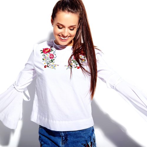Portrait of beautiful caucasian smiling brunette woman model in white blouse and summer stylish blue jeans with flowers print isolated on white background