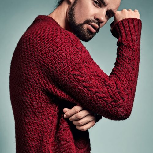 portrait of handsome fashion stylish hipster lumbersexual model dressed in warm red sweater  posing in studio. Metrosexual
