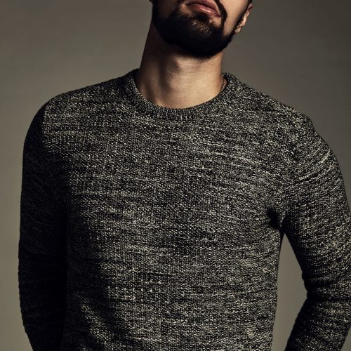 portrait of handsome fashion stylish hipster lumbersexual model dressed in warm sweater  posing in studio. Metrosexual