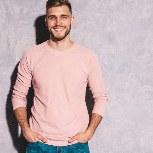 Portrait of handsome smiling hipster lumbersexual businessman model wearing casual summer pink clothes. Fashion stylish man posing against gray wall